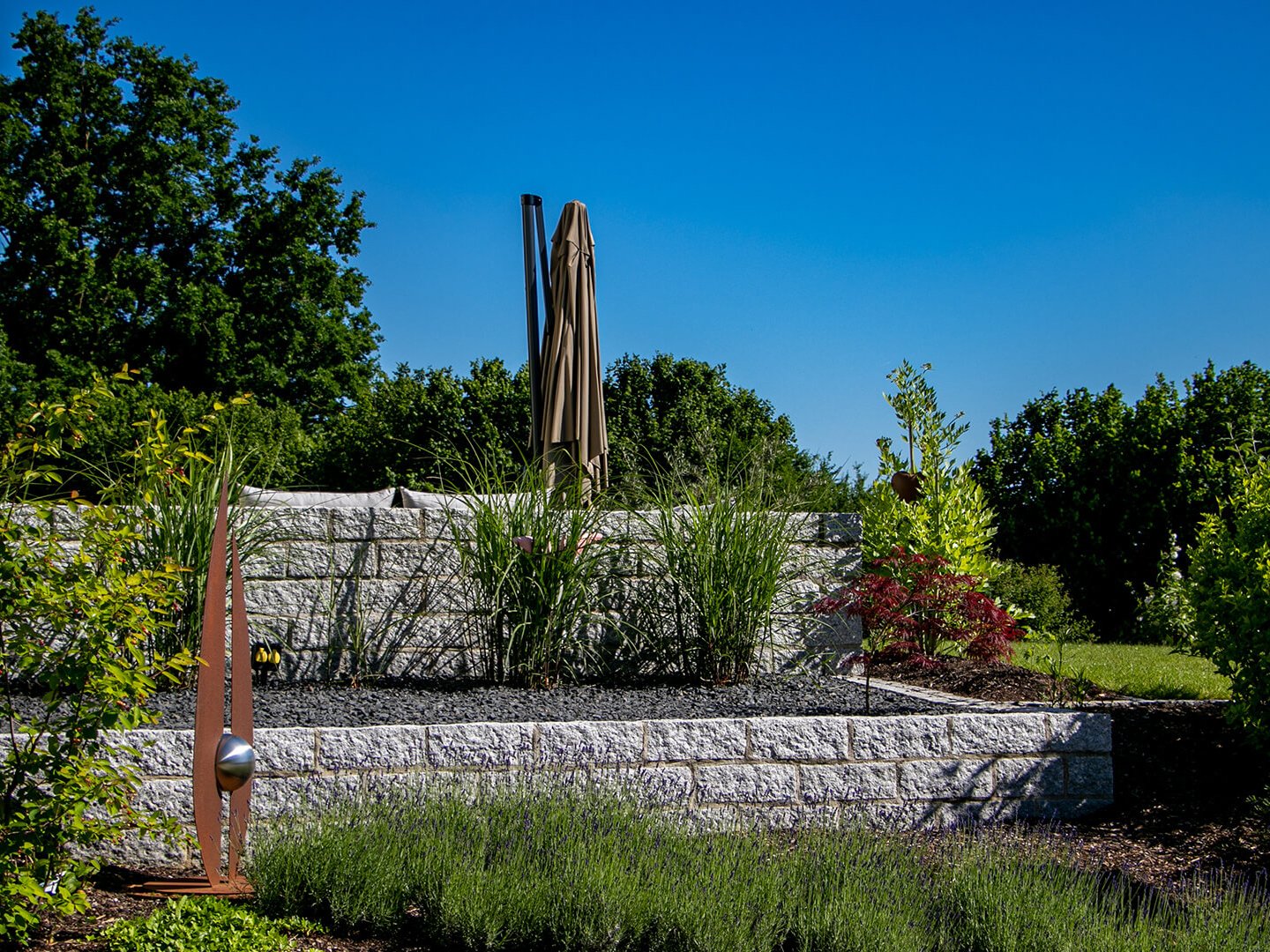 Granitmauer mit Bepflanzung und Kunstelement